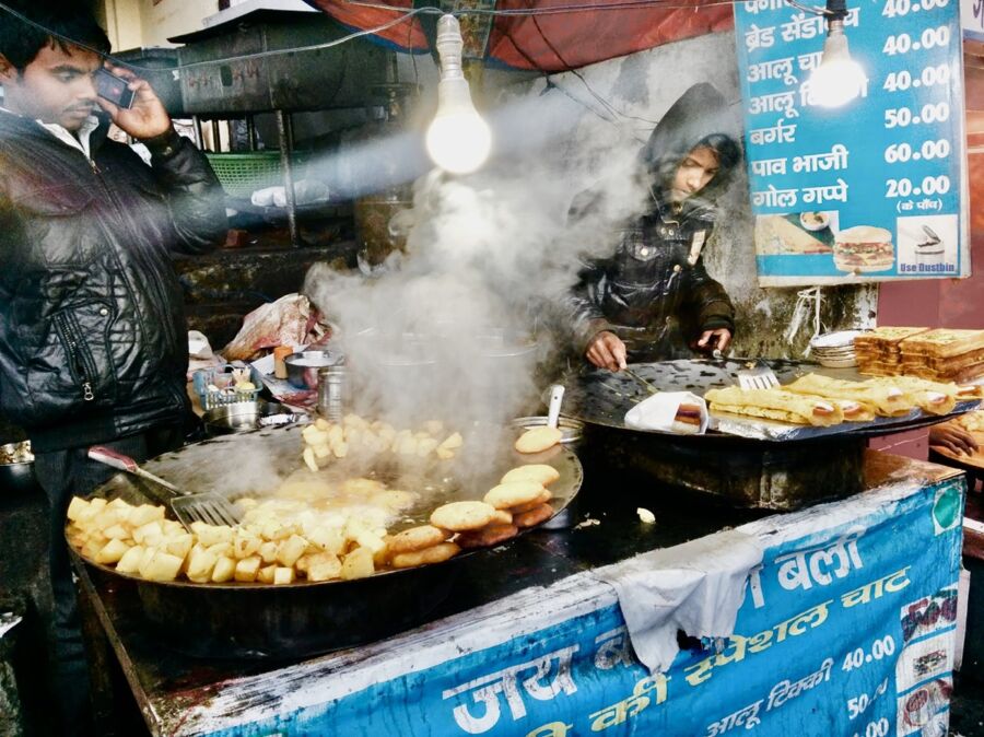 Vibrant street food market with vendors frying golden fritters and potatoes in chilly air.