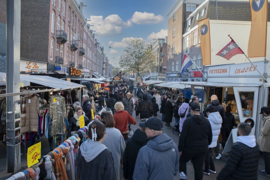 Busy European street market on a chilly autumn day, crowded shoppers buying clothes and street food.
