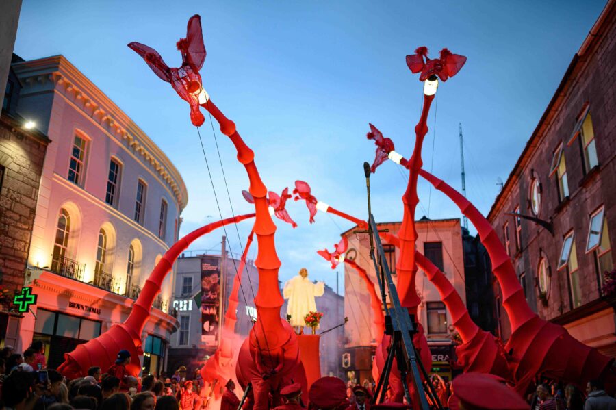Galway Arts Festival street performance with giant red puppets and crowd at dusk.