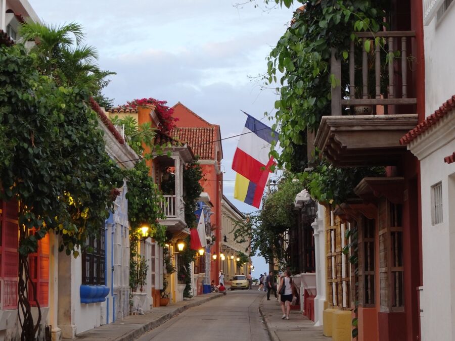 Historic cobblestone street with colorful colonial buildings, vibrant flags, and evening ambiance.