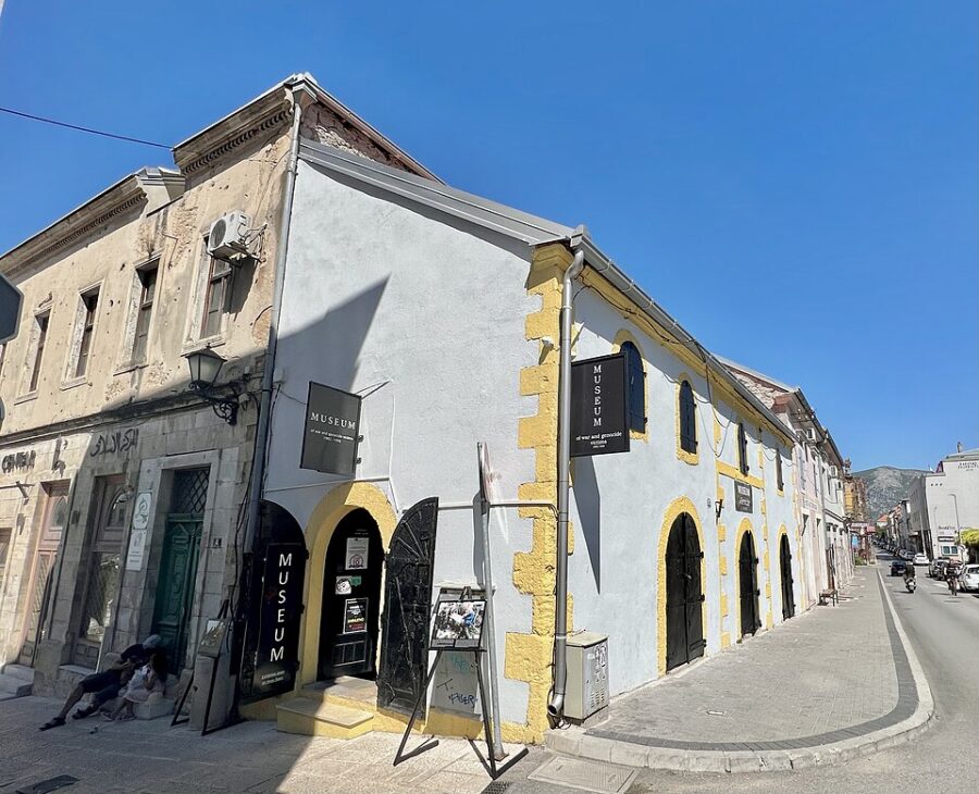 Charming street with diverse architecture: modern museum, historic building, pedestrians, scenic mountains.