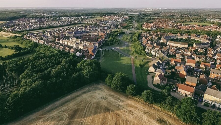 Aerial view of suburbia blending homes, park, and fields with distant urban skyline.