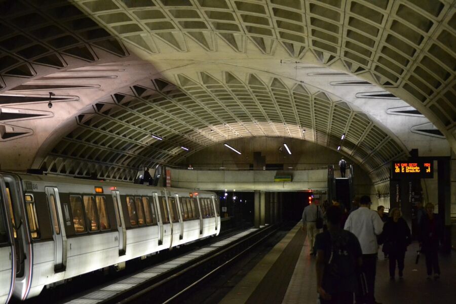 Modern subway station with architectural design, ambient lighting, streamlined train, and diverse commuters.