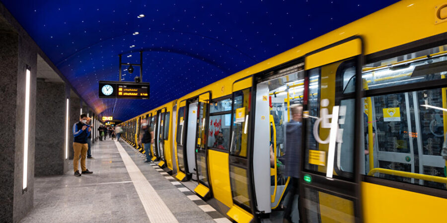 Modern subway station with glass panels, yellow trains, and digital clock.