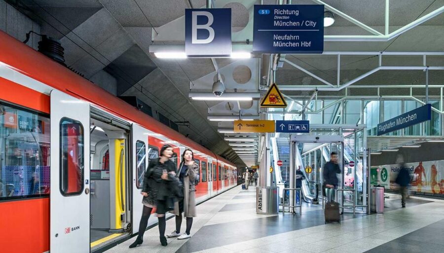 Munich train station: sleek architecture, red train, commuters heading to city and airport.