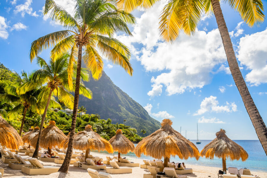 Beautiful Sugar Beach in Saint Lucia, showcasing palm trees, straw umbrellas, and the majestic Gros Piton mountain behind