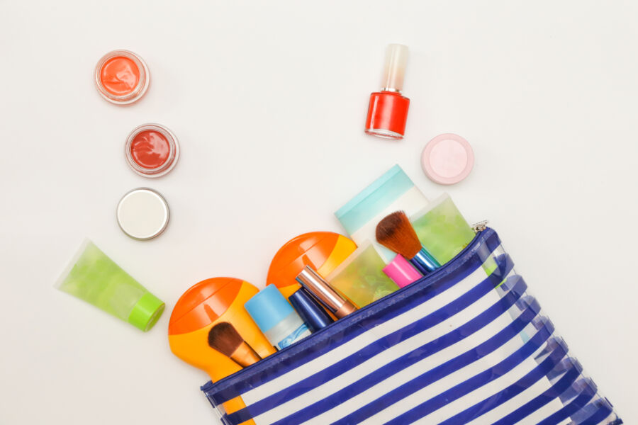 Striped cosmetic bag spills assorted makeup items, including brushes, lipstick, nail polish, and cream jars, against a clean, white background.