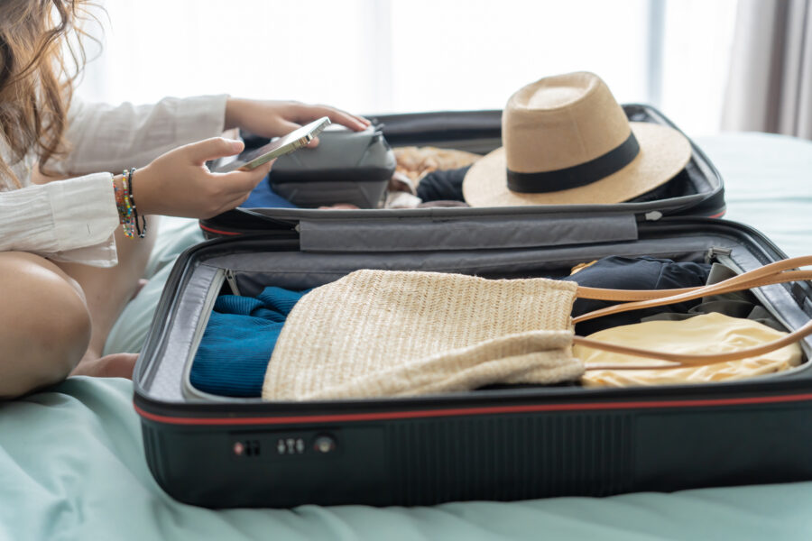 Woman arranging clothes in a suitcase on a bed, with a packing list visible, ready for her upcoming travel adventure