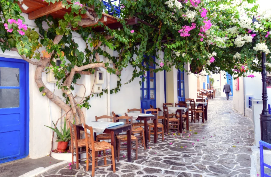 Milos, Greece: sunlit alley cafe with blue doors and bougainvillea.