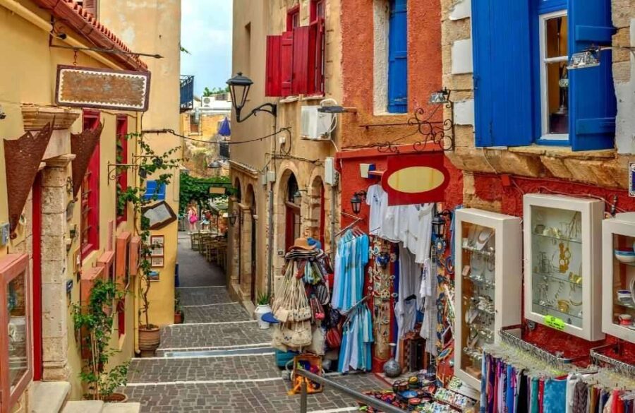 Sunlit cobblestone alley in Chania Old Town, Crete, lined with Mediterranean shops and cafes.