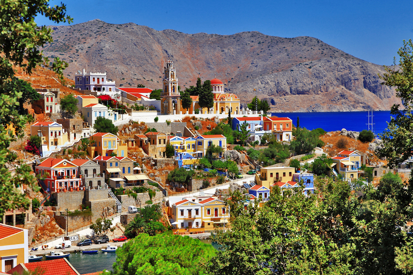 Sunlit Symi harbor with colorful Greek island houses and Aegean sea views.