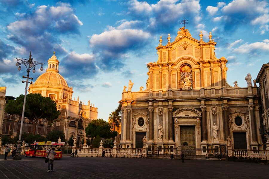 Sunlit historic Baroque plaza in Catania, Sicily featuring cathedral facade and dome.