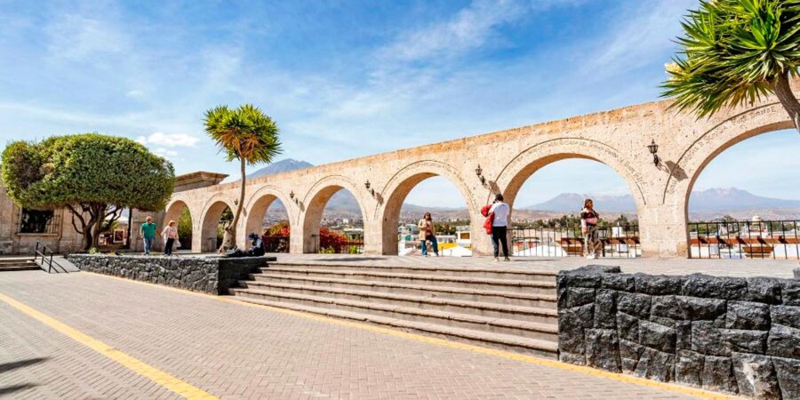 Sunny Yanahuara stone arches viewpoint plaza overlooking Arequipa city and distant Andean mountains.