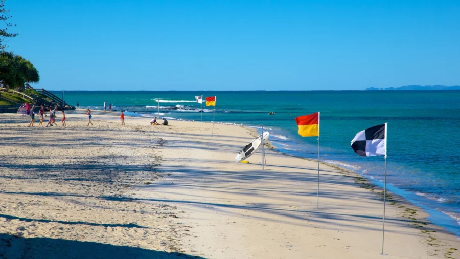 Sunny lifeguard‑patrolled sandy beach with safety flags, calm turquoise ocean, clear blue sky.