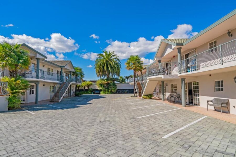 Sunny Rotorua motel courtyard with palm trees, parking area, balconies, and spa-style accommodation.