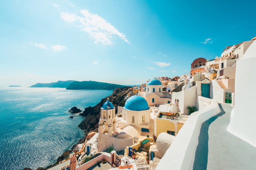 Scenic view of Oia, Santorini, featuring sunlit white buildings and iconic blue domes under a vibrant blue sky