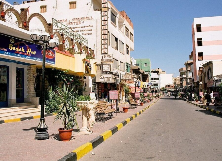 Sunny Dahar shopping street with beach shops, restaurants, palm plants and tourist pedestrians.