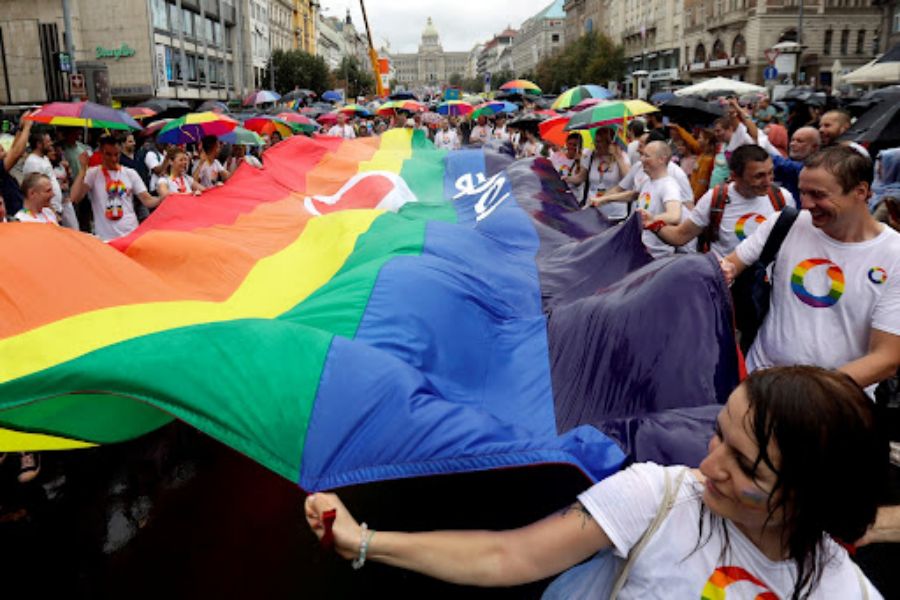 Pride parade in Prague: diverse crowd, rainbow flag, colorful umbrellas, urban backdrop, LGBTQ+ celebration.