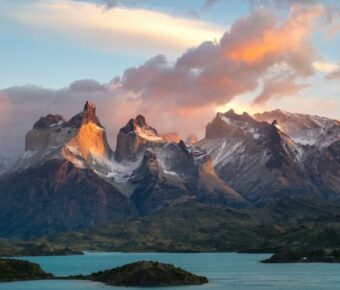 Sunrise over jagged snow-capped mountains reflected in a turquoise alpine lake landscape.