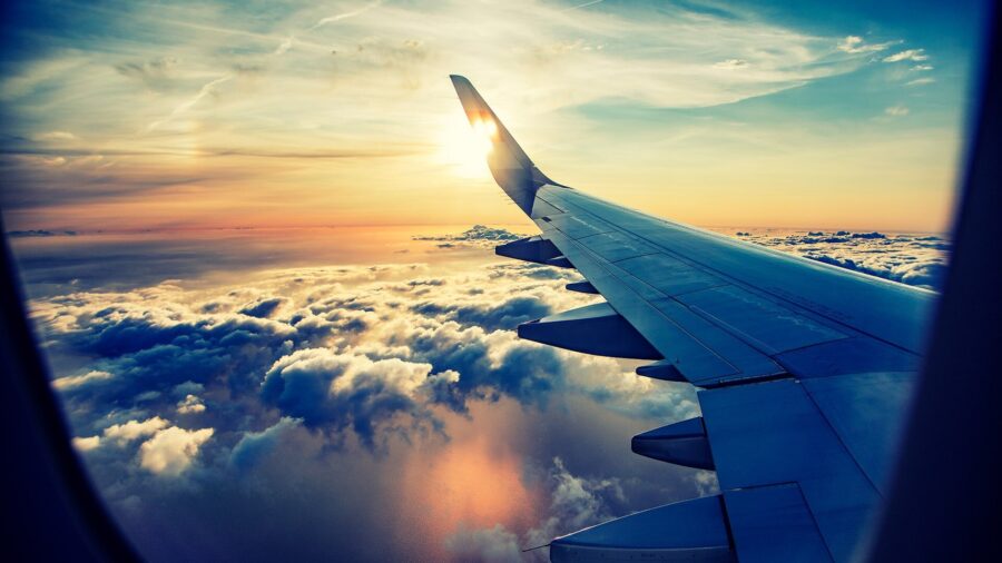 Airplane wing view at sunset over clouds, showcasing sky colors and aerial travel beauty.