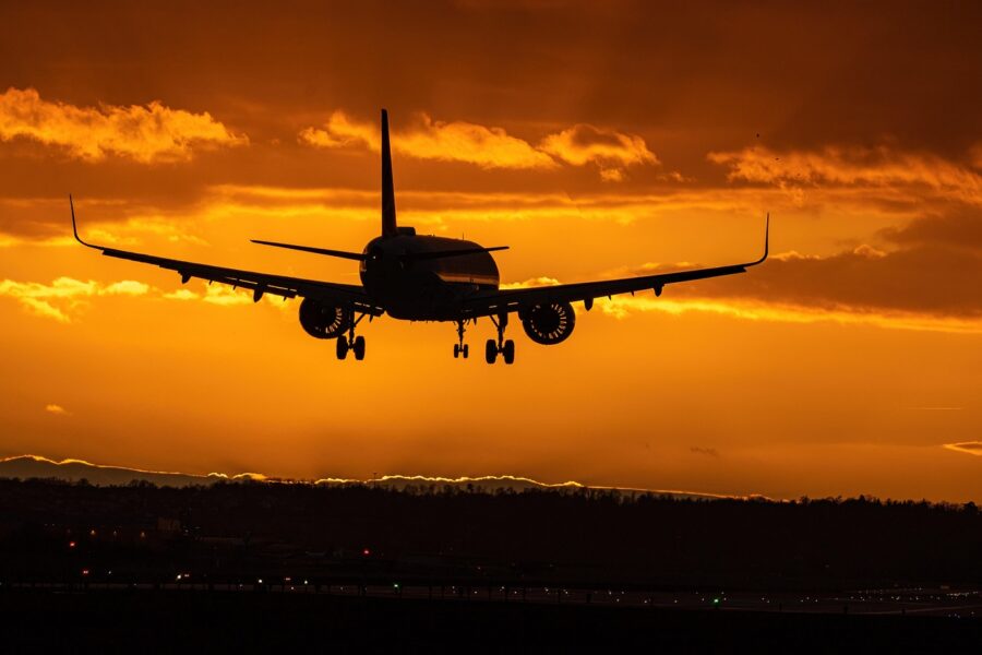 Silhouette of airplane landing against a colorful sunset sky.