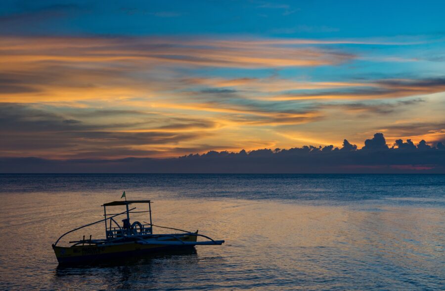 Sunset outrigger boat on calm tropical Camiguin seascape with dramatic colorful sky.