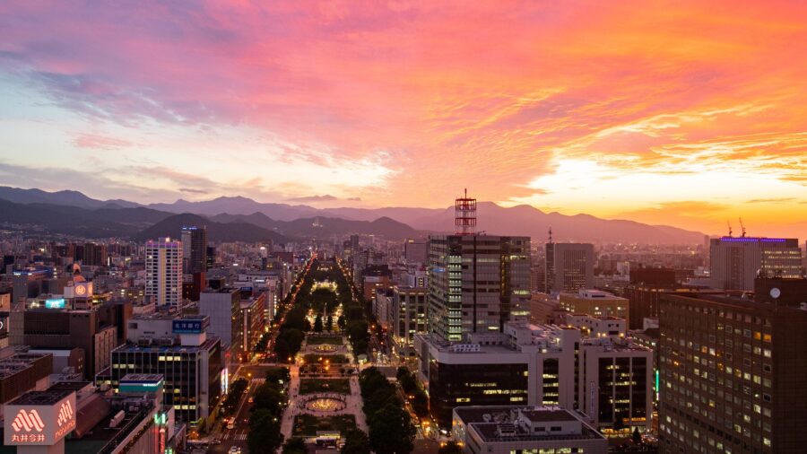 Sunset cityscape with tree-lined boulevard, park, traffic lights and mountain skyline in Hokkaido.