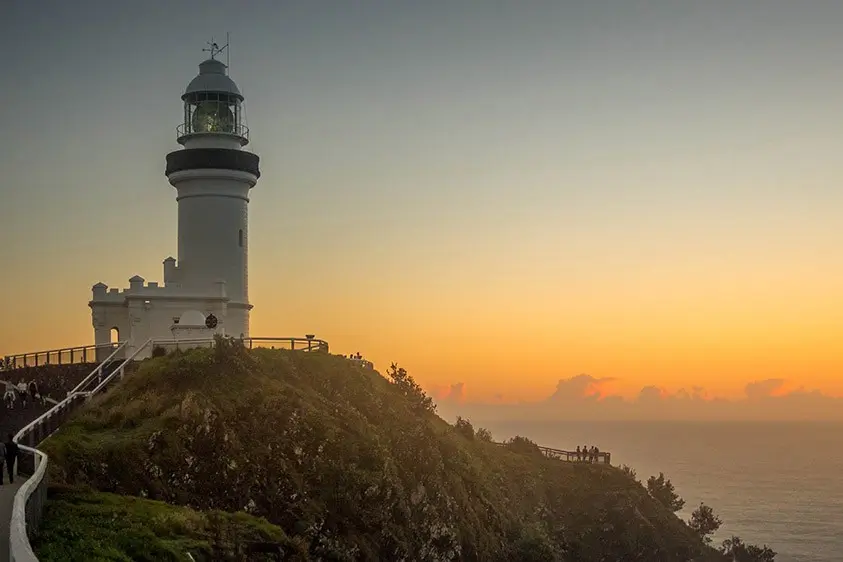 Cape Byron Lighthouse at sunset on coastal cliff, ocean lookout with tourists enjoying scenic views.