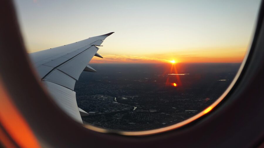 Airplane wing at sunset with scenic landscape view below.