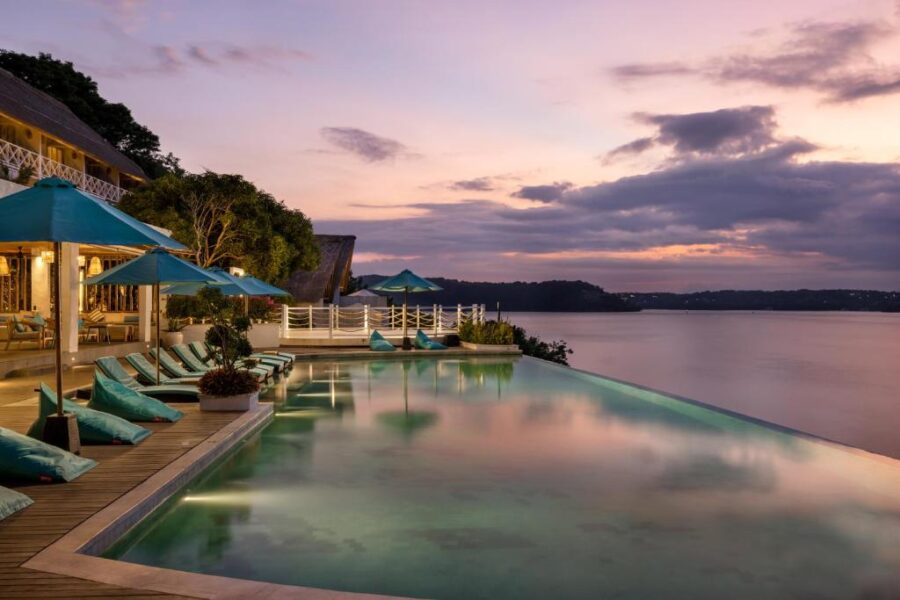 Luxury Nusa Penida infinity pool resort at sunset with ocean view, loungers, umbrellas, and sky.
