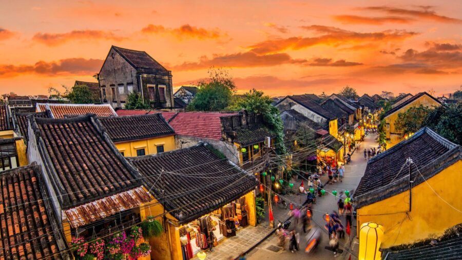 Sunset over Hoi An old town rooftops and lantern-lit street market in Vietnam.