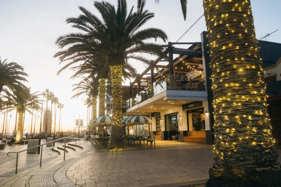 Beachfront bar and restaurant promenade at sunset with palm trees, fairy lights and ocean views.
