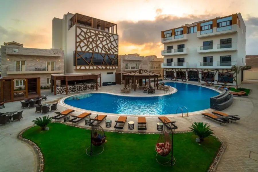 Luxury resort pool courtyard at sunset with gazebo, lounge chairs, modern hotel buildings, and palm landscaping.