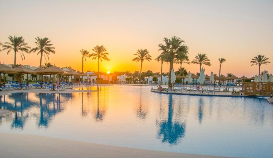 Luxury resort infinity pool at tropical sunrise with palm trees, sun loungers, and calm water reflections.