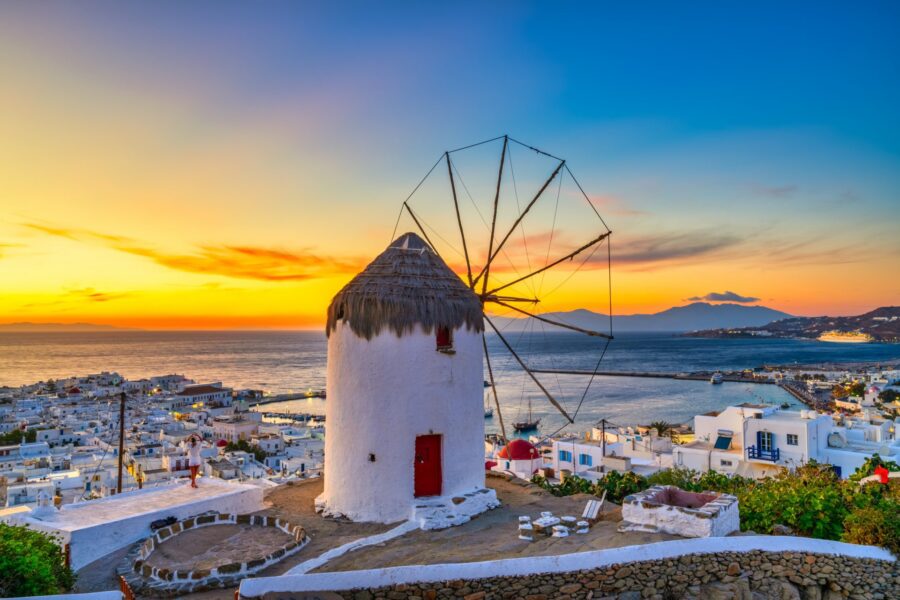 Sunset over Mykonos windmill overlooking coast, representing Mediterranean charm and cultural heritage.