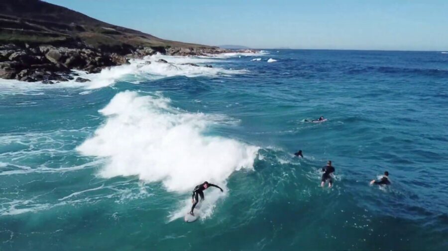 Surfer carving a breaking wave off the Laxe coastline, other surfers waiting in the ocean.