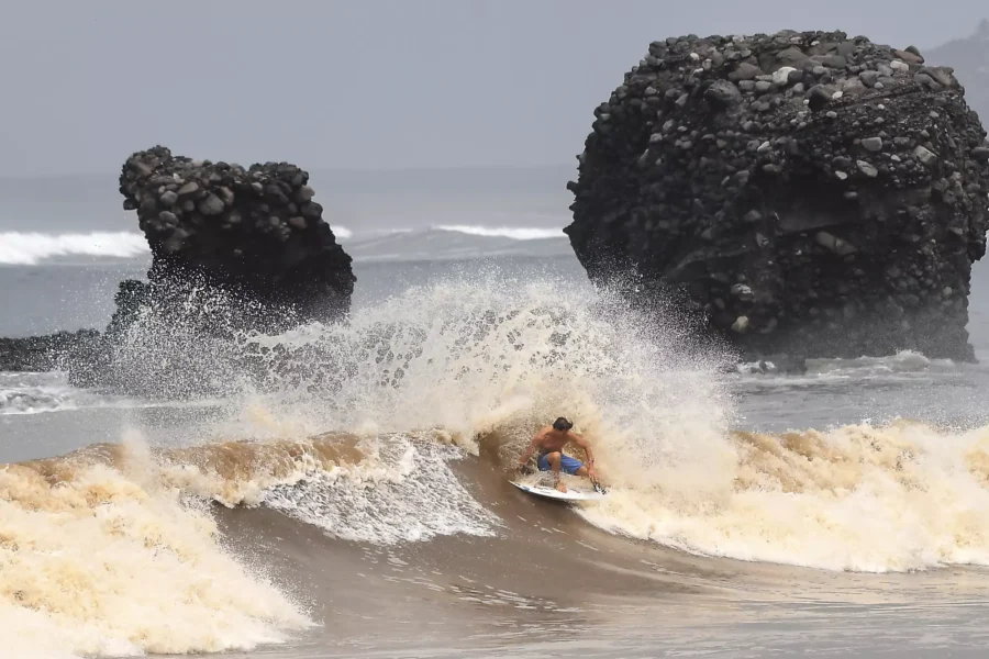 Surfer riding powerful wave at El Tunco beach, framed by dramatic rock formations.