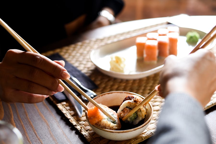 Two people enjoying fresh sushi rolls with chopsticks, showcasing vibrant colors and textures.