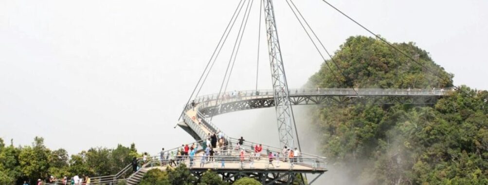 Modern suspension bridge with tourists, offering panoramic views over lush green landscape.