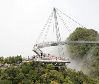 Modern suspension bridge with tourists, offering panoramic views over lush green landscape.