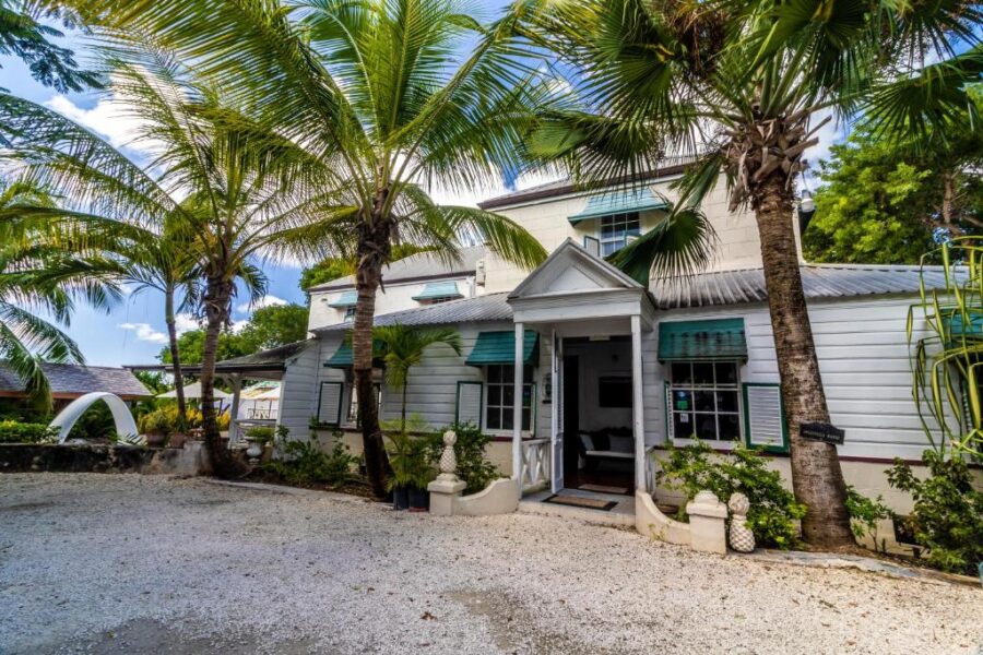 Sweetfield Manor in Barbados, showcasing a white house with palm trees and a spacious driveway.