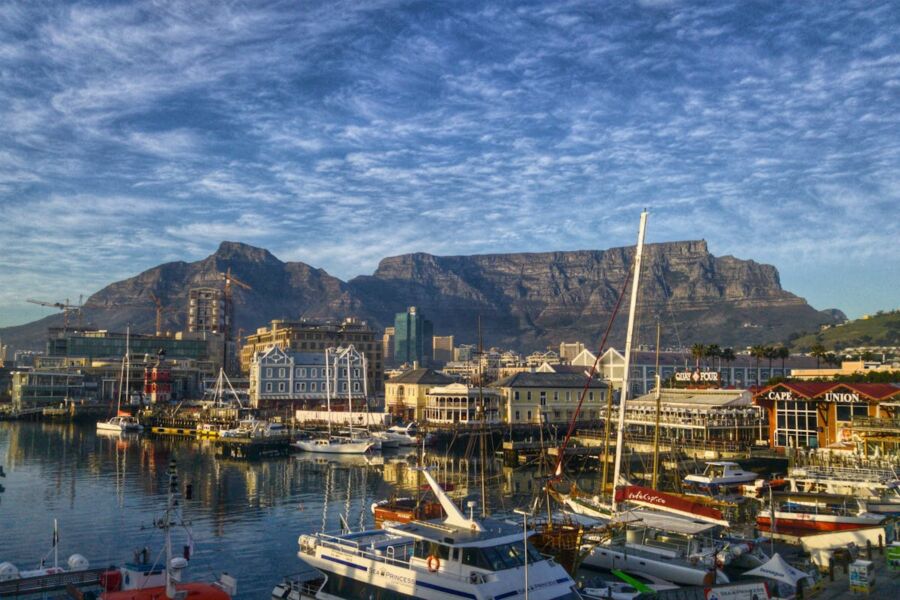 Cape Town waterfront with yachts, Table Mountain, vibrant architecture under a cloudy sky.