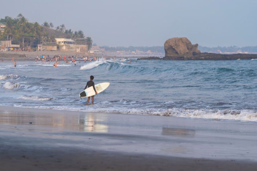 View of a surfer at Tamarindo Beach, Costa Rica, with a colorful sunset and tropical palm trees surrounding the scene