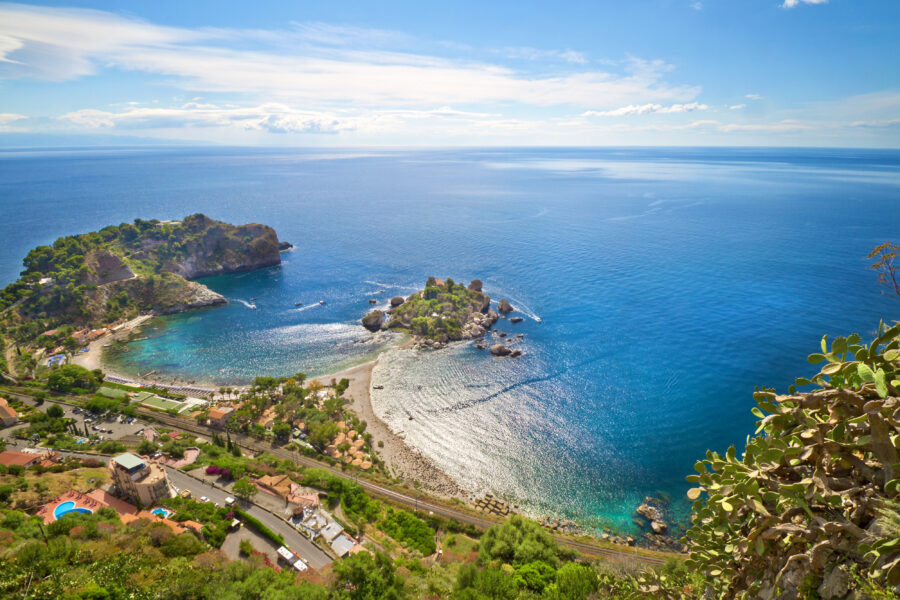 Panoramic view of Taormina's coastline in Sicily, showcasing cliffs, turquoise sea, and lush greenery