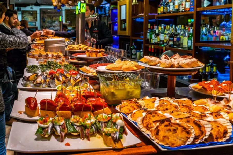 San Sebastián tapas bar with assorted pintxos, seafood, roasted peppers, and toasted bread.