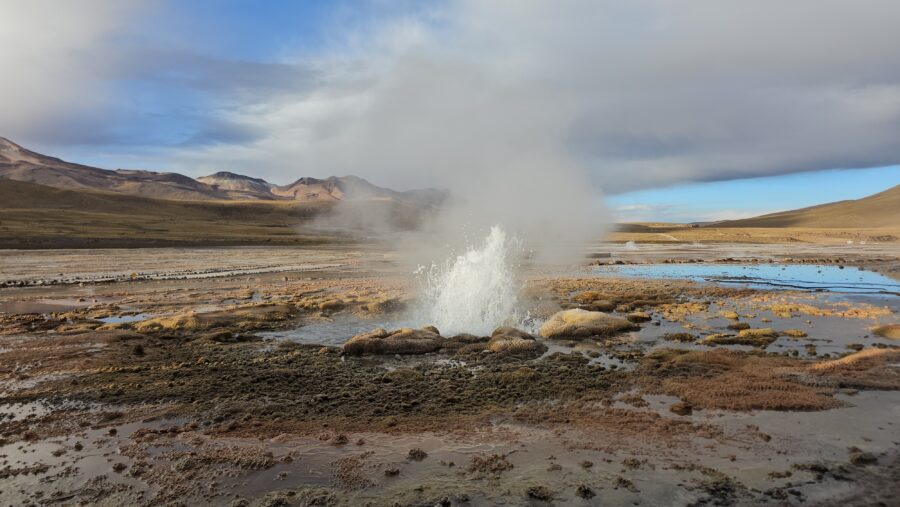 Tatio Geysers in Chile, showcasing a geyser erupting amidst the vast, dry desert terrain.
