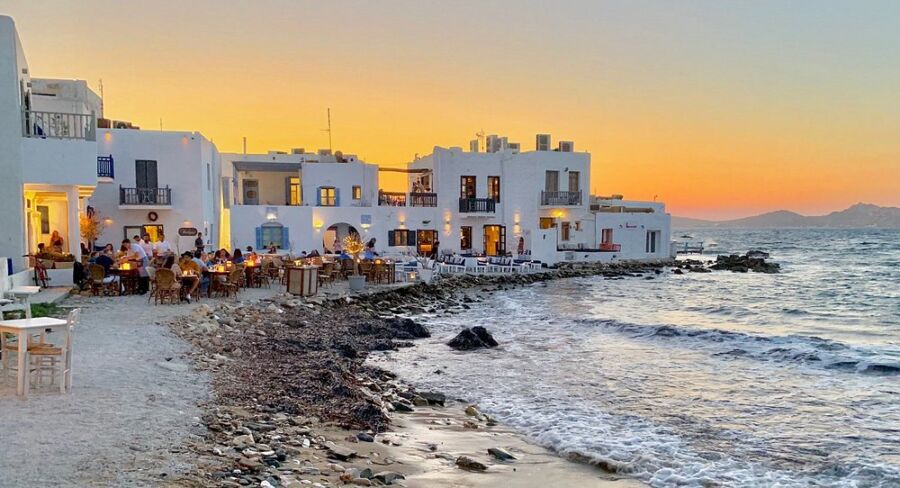Sunset over the beach and restaurant of Taverna Glafkos in Paros, Greece, with vibrant colors reflecting on the water and silhouettes of distant hills.