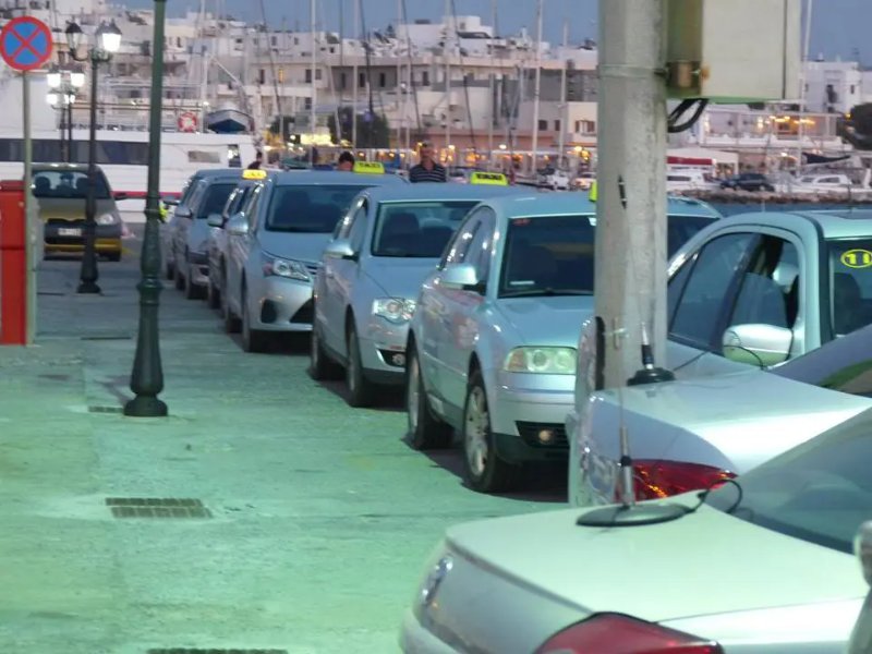 Harbor taxi queue at dusk with silver taxis and illuminated TAXI signs by marina.