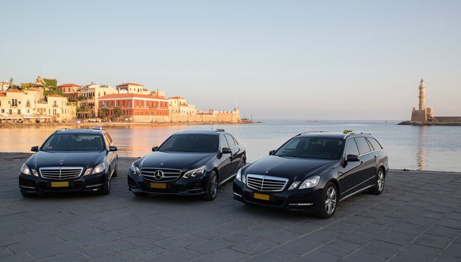 Chania harbor black Mercedes taxis lined on waterfront promenade at sunrise with lighthouse backdrop.