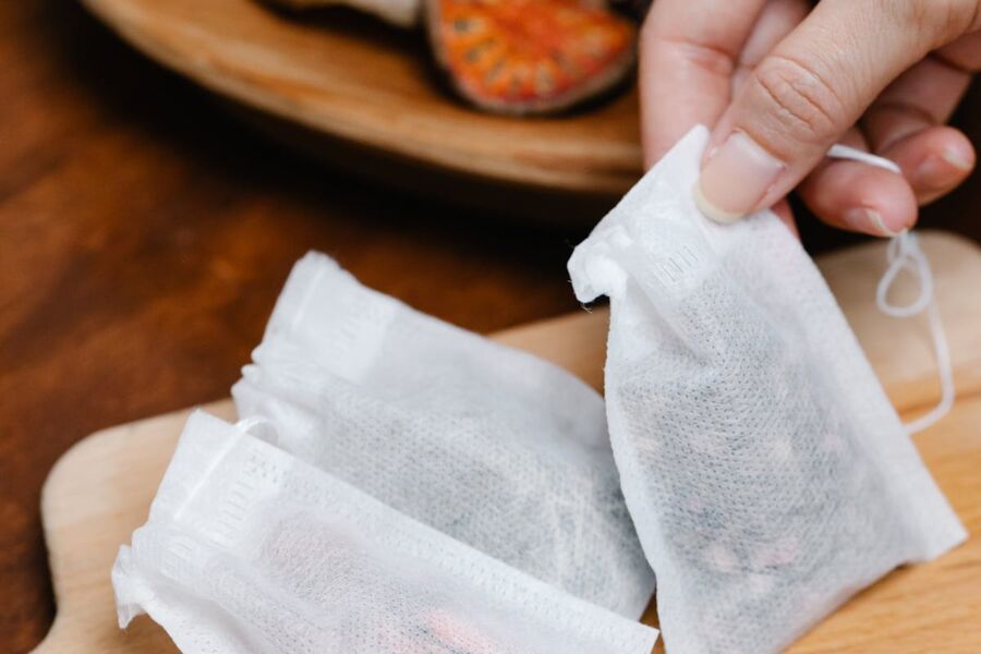 Hand holding herbal tea bags on wooden board with dried orange slice.